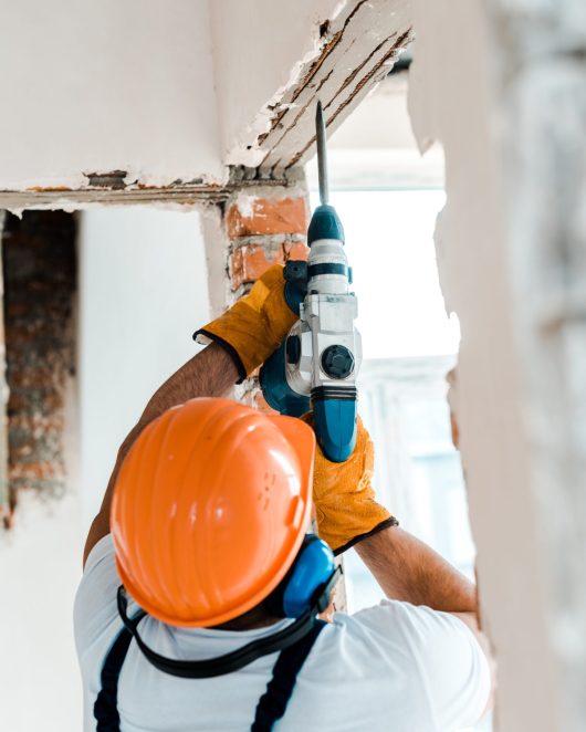 back view of handyman using hammer drill on wall