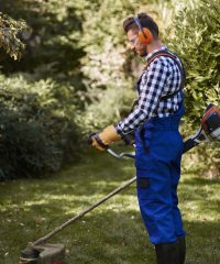 Busy man using a weedwacker at garden